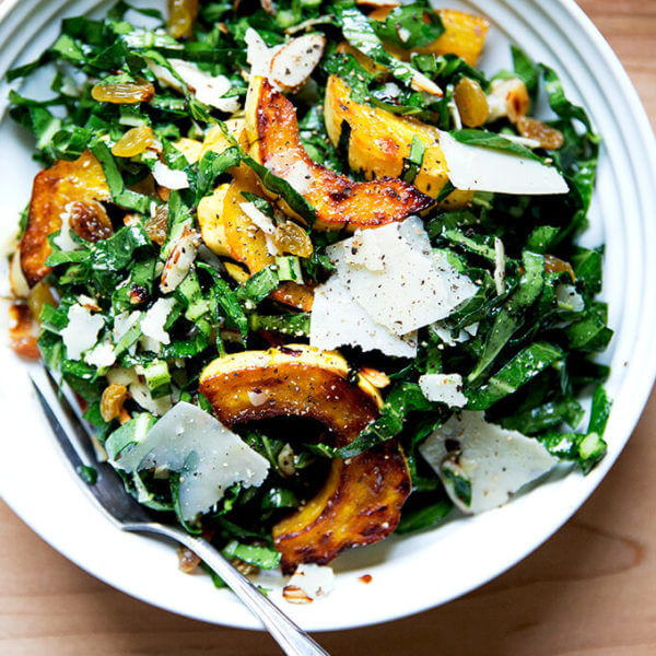 A bowl of raw collard green salad with roasted delicata squash, toasted almonds, golden raisins, and shaved parmesan.