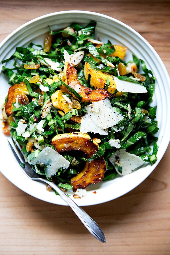 A bowl of raw collard greens salad with roasted delicata squash, shaved parmesan, toasted almonds and golden raisins. 