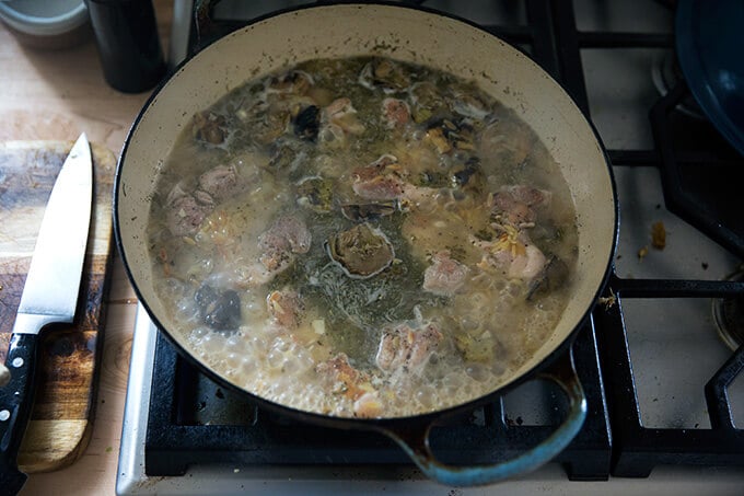 A skillet of one-pan lemon chicken orzo with artichoke hearts simmering.