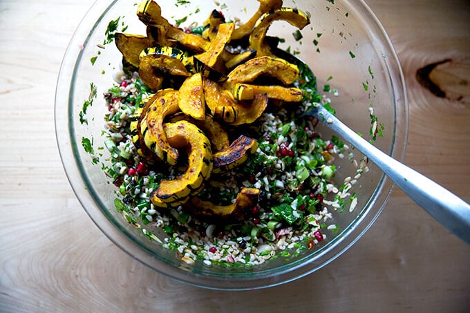 An overhead shot of a glass bowl filled winter tabbouleh and roasted delicata squash.