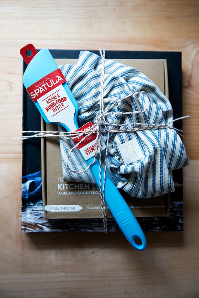 A wrapped gift set: Bread Toast Crumbs, a spatula, a cloth bowl cover, a scale, and a card.