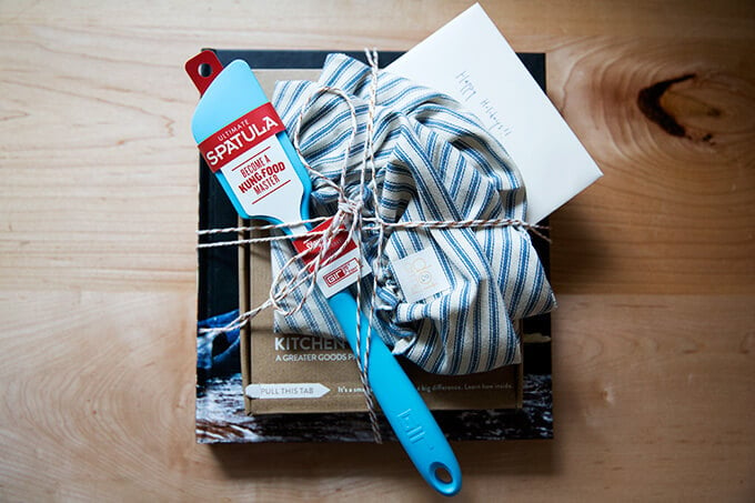 A wrapped gift set: Bread Toast Crumbs, a spatula, a cloth bowl cover, a scale, and a card.