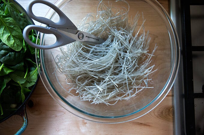 A large bowl filled with soaked and drained sweet potato noodles with scissors.