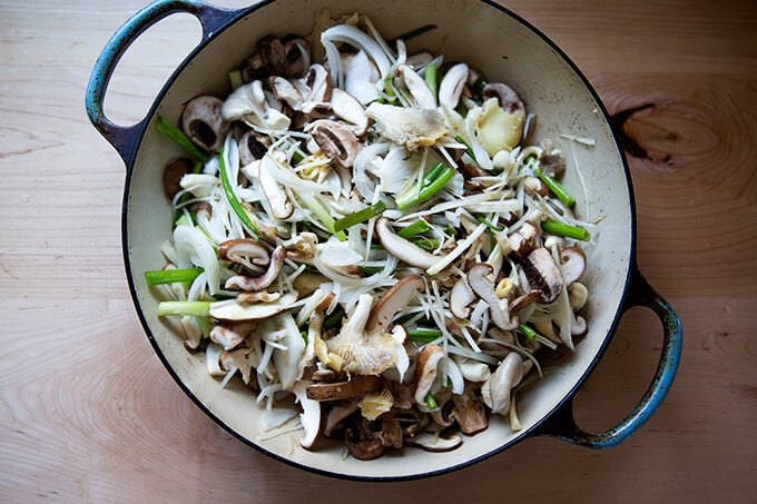 A braiser filled with mushrooms, scallions, onions, and carrots.