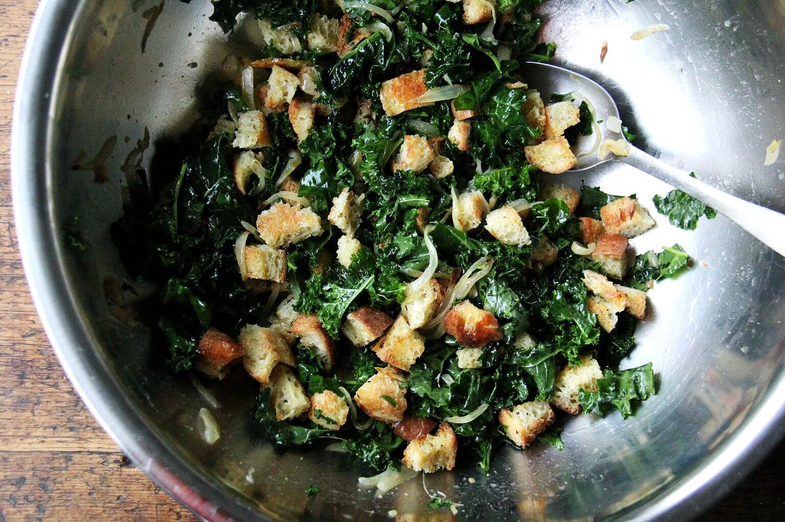 A large bowl filled with toasted cubes of peasant bread tossed with kale and caramelized onions.