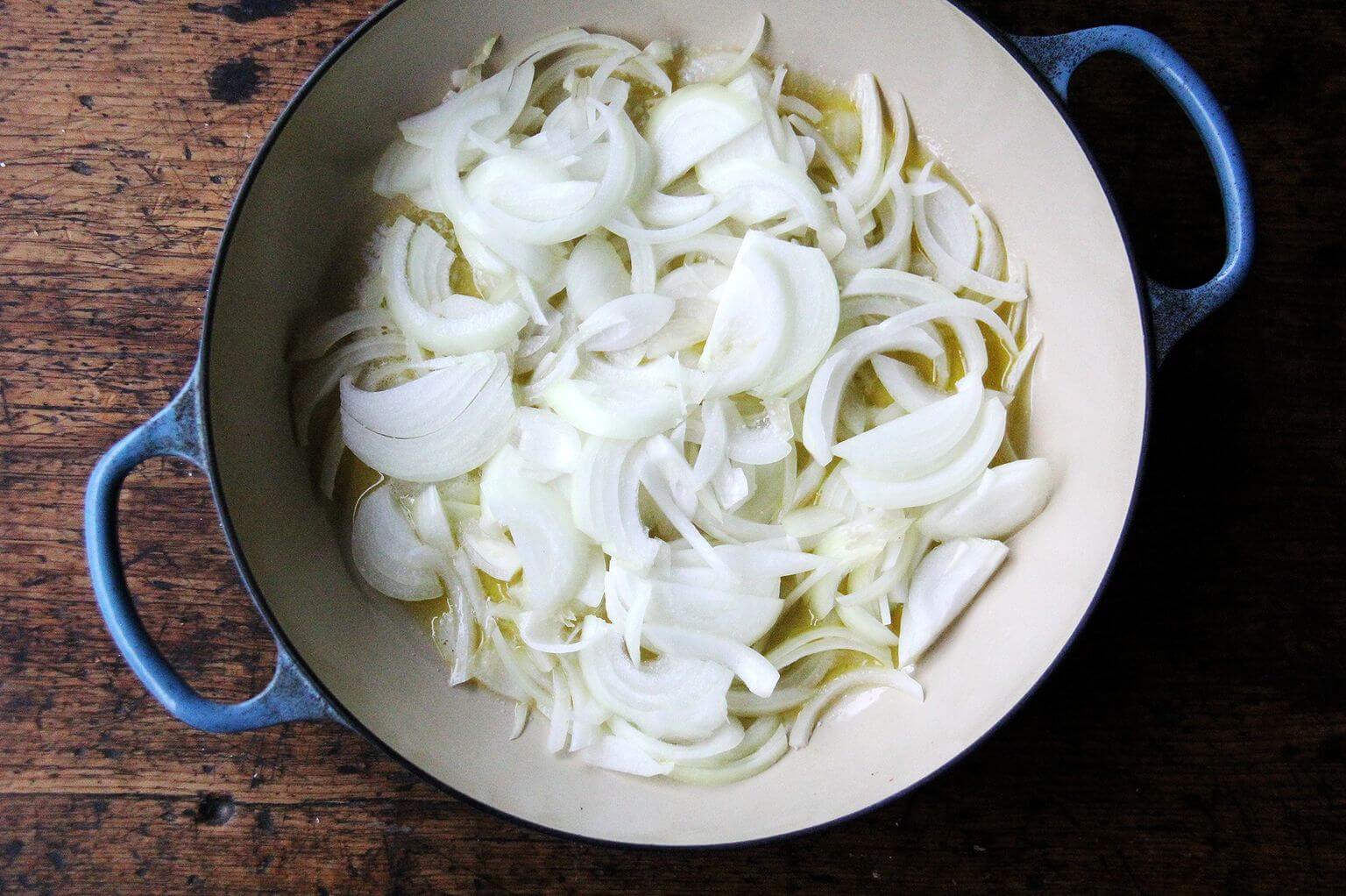 A sauté pan with onions and olive oil.