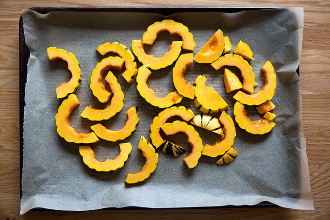 A sheet pan lined with parchment paper spread with delicata squash slices, olive oil, and salt.