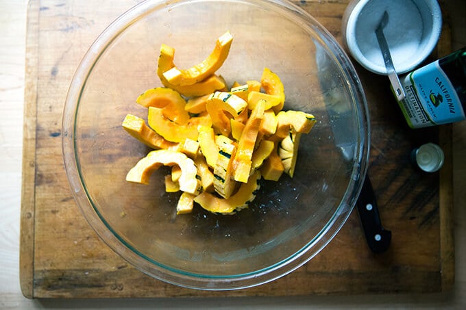 A large glass bowl filled with delicata squash slices, olive oil, and salt.