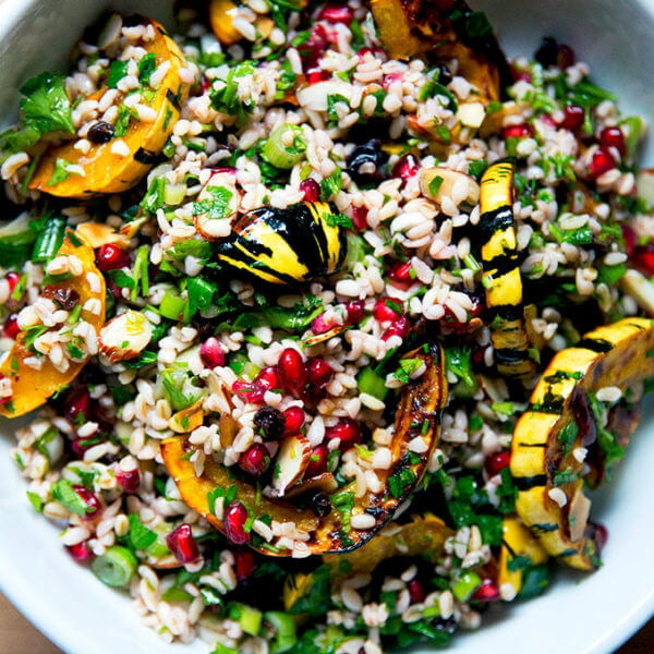 A white serving bowl filled with winter tabbouleh and roasted delicata squash slices.