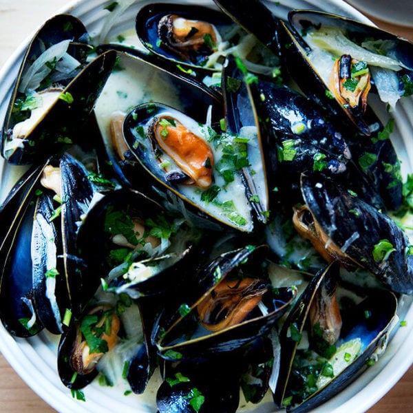 A bowl of steamed mussels aside bread.