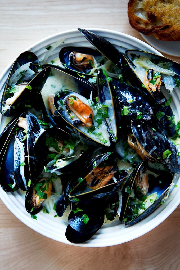 A bowl of steamed mussels aside bread.