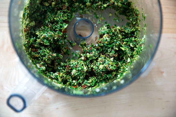A food processor holding the puréed ingredients to make sun-dried tomato pesto.