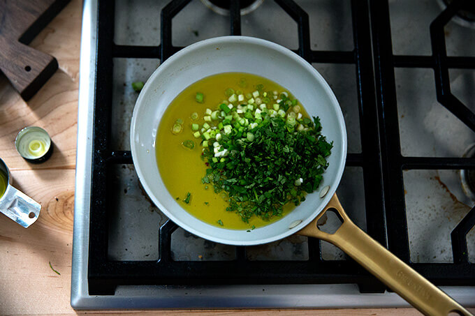 A small skillet holding oil, scallions, and cilantro.