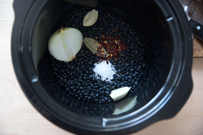 Overhead shot of dried black beans with aromatics in a slow cooker.
