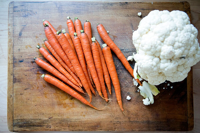 A board with whole carrots and a head of cauliflower.