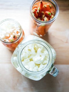Overhead shot of pickled carrots and cauliflower in glass jars.