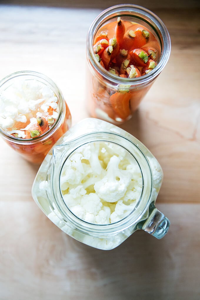 Overhead shot of pickled carrots and cauliflower in glass jars.