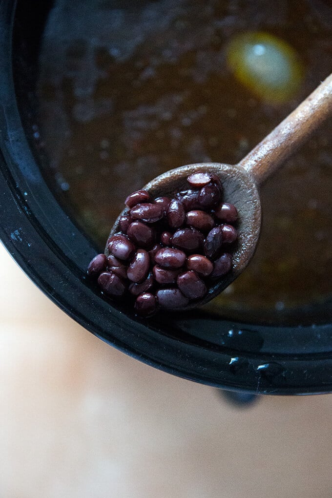 A wooden spoon holding cooked slow cooker black beans.