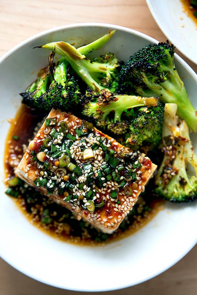 A bowl of tofu with spicy sesame scallion sauce aside spicy broiled broccoli.