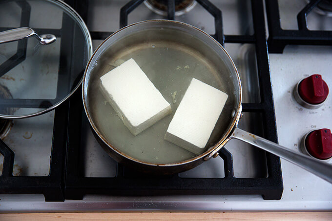 A halved block of tofu simmering in water.