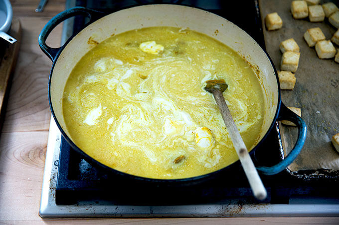 A skillet stovetop with onions, curry spices, coconut milk and water.