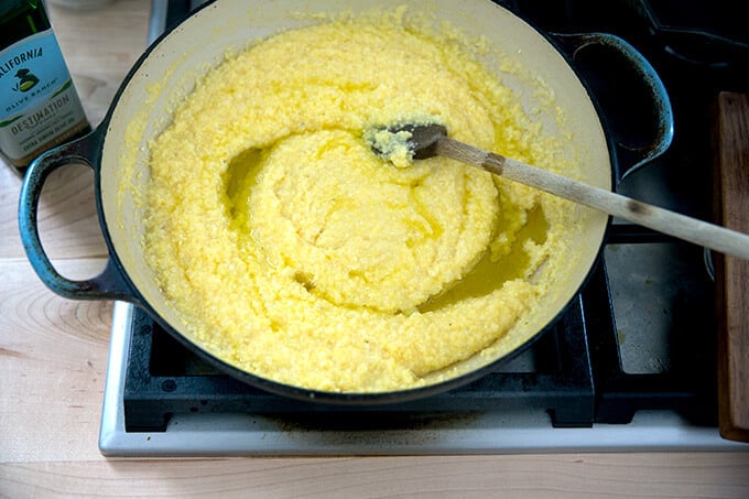 A skillet of cooked polenta with olive oil being stirred in.