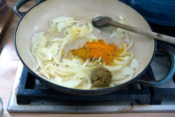 A skillet with onions, curry powder, turmeric, and Thai green curry paste.