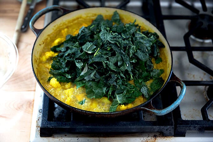 A vegetable curry simmering stovetop with a heap of kale on top.