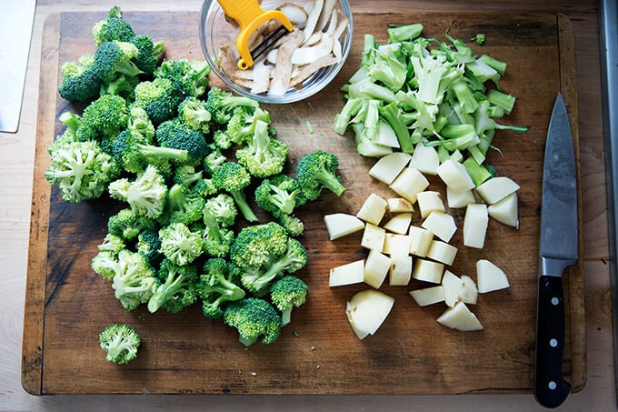 A board with broccoli florets, cubed potatoes, and broccoli stems.