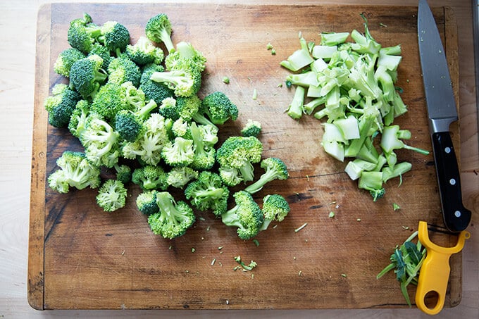 An overhead shot of a cutting board with broccoli florets and stems.