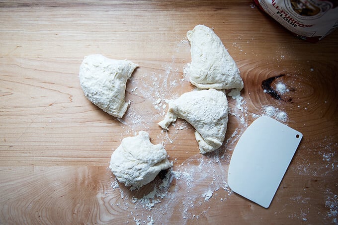 Four portions of naan dough on a floured work surface.