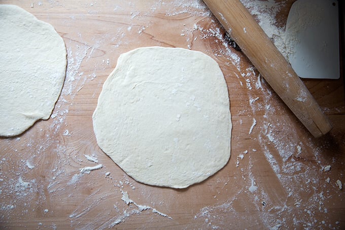 Two rounds of naan rolled out onto a floured work surface.