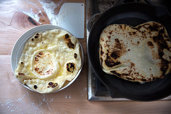 A skillet of naan being cooked aside a freshly cooked naan in a bowl.