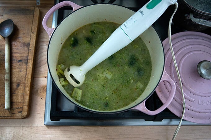 A Dutch oven with an immersion blender puréeing broccoli-cheddar soup.