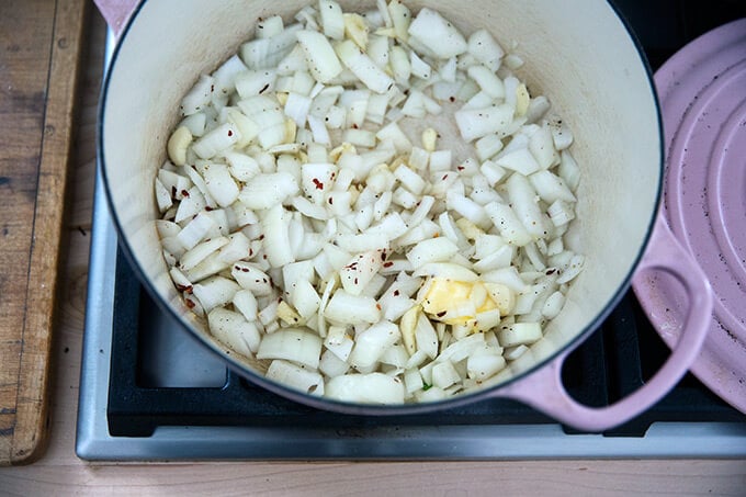 A Dutch oven with onions, garlic, crushed red pepper flakes, and butter.