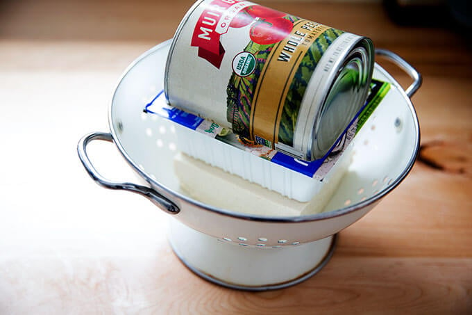 Tofu, being pressed in a colander.