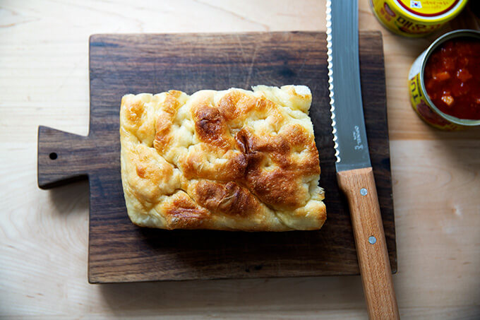 A loaf of stale focaccia on a board with a knife.