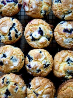 An overhead shot of a dozen blueberry muffins on a cooling rack.