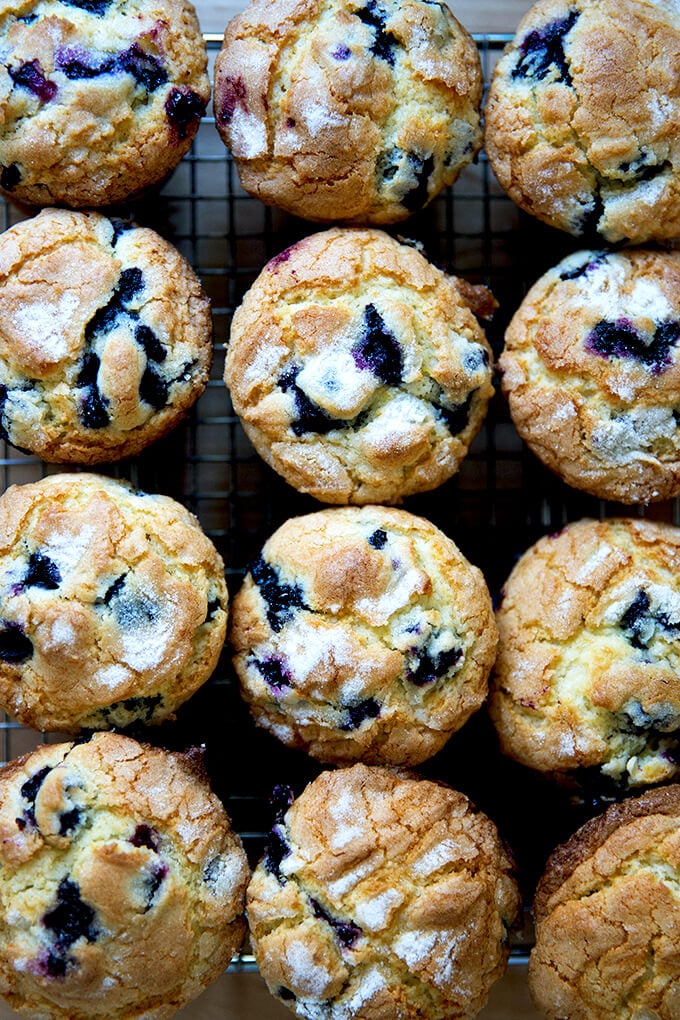 An overhead shot of a dozen blueberry muffins on a cooling rack.