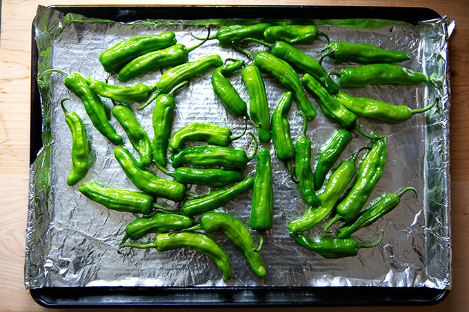 A sheetpan lined with foil, topped with shishito peppers tossed in olive oil and seasoned with salt.