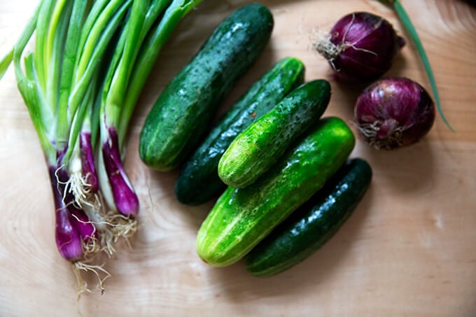 Scallions, cucumbers, and red onions on a board.