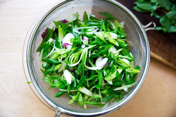 Drained scallions in a sieve.