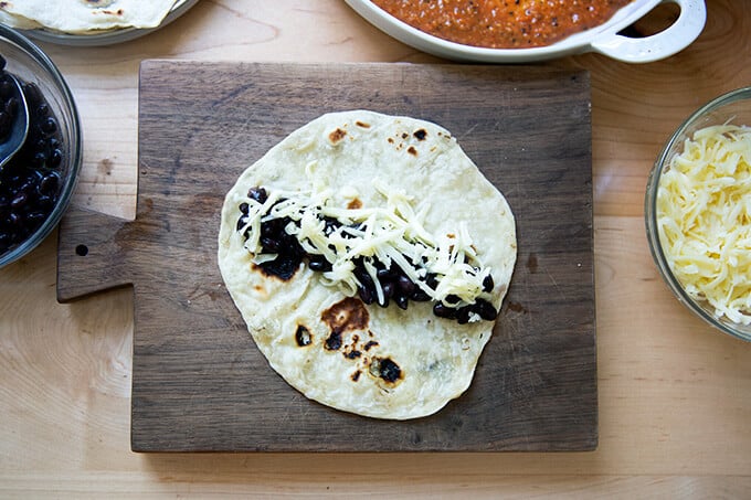 A flour tortillas on a board with black beans and cheese over top.