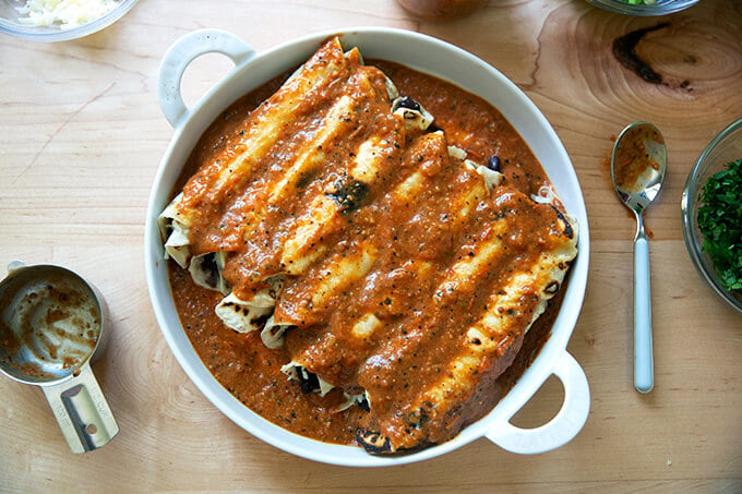 A dish filled with enchiladas, topped with enchilada sauce.