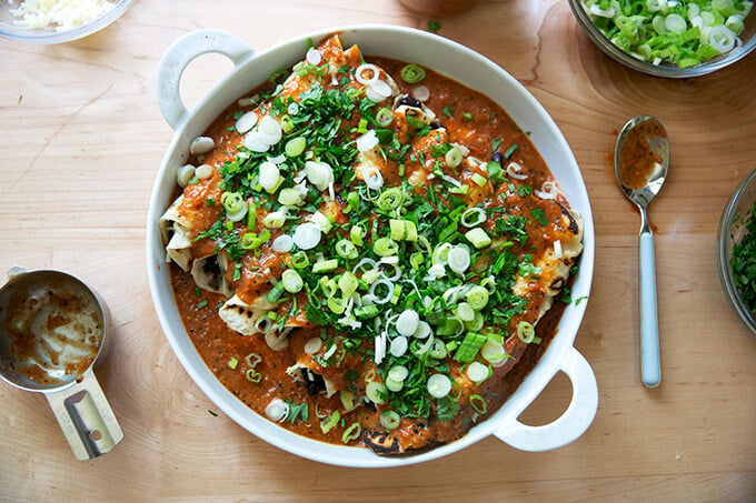 A baking dish filled with enchiladas, topped with sauce, scallions, and cilantro.