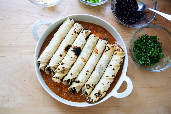 A baking dish filled with tortillas rolled with black beans and Monterey Jack cheese.