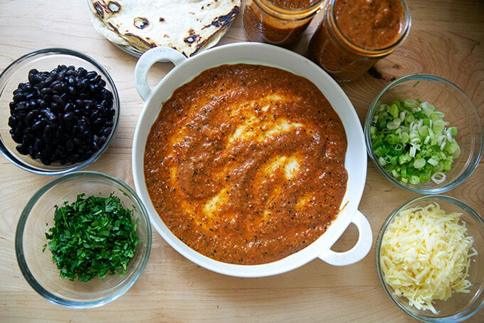 A baking dish filled with red enchilada sauce, surrounded by ingredients to make black bean and cheese enchiladas.