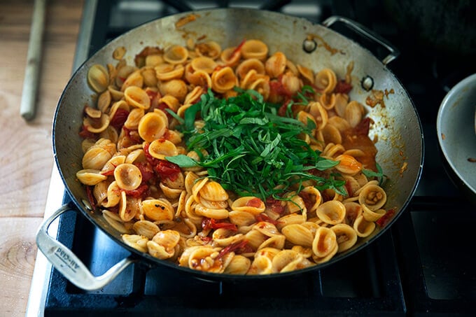 A skillet of pasta on the stovetop with basil added.