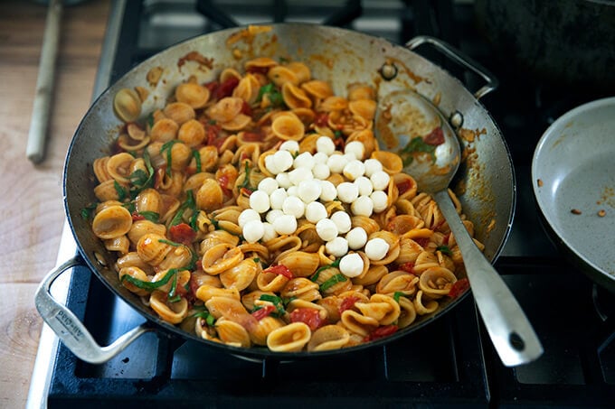 A skillet of pasta on the stovetop with fresh mozzarella added.