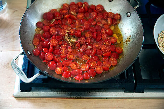 A skillet on the stovetop with shallots, garlic, olive oil, and tomatoes.